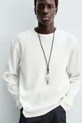 Camiseta blanca de manga larga con cuello redondo y textura cuadriculada.