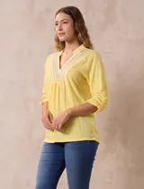 Blusa blanca de poliéster y rayón con escote en V bordado y mangas tres cuartos regulables con presilla y botón.