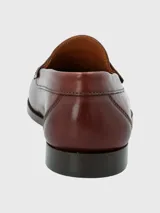 Zapato mocasín de cuero color marrón, con detalle de antifaz y suela de cuero y goma.