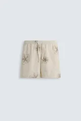 Bermuda regular fit color beige con bordados de flores en tono marrón. Tiene cintura elástica ajustable con cordón, bolsillos laterales y un bolsillo trasero de plastrón.
