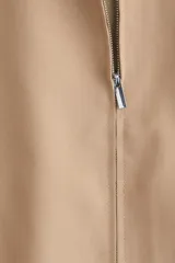 Campera color beige de sarga con cuello, cierre oculto adelante y bolsillos laterales con cierre. Modelo de corte holgado con pinzas en los codos para dar forma y cordón para ajustar elástico con topes en el bajo. Sin forrar.