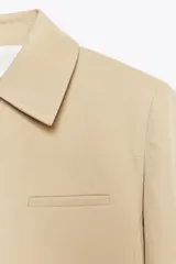 Chaqueta color beige de cuello solapa y manga larga con hombreras acabada en puño. Presenta bolsillos laterales y falso bolsillo de vivo en pecho. Cierre frontal con botones.