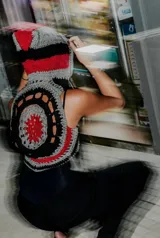 Chaleco negro de cuero con apliques de crochet en tonos grises y rojos.