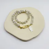 Collar elaborado con cuentas de Piedra de la Luna de 8 mm de diámetro, separadas por nuditos de hilo color caramelo. El cierre es de acero hipoalergénico con baño dorado y tiene un dije de nácar en forma de pez.