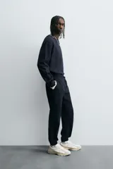 Pantalón jogger negro de corte slim fit, confeccionado en tejido de algodón con cintura elástica ajustable con cordón, bolsillos frontales y traseros de vivo, y bajo con puño elástico.