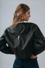 Campera bomber color beige de cuero, con cuello redondo, cierre frontal con botones a presión, mangas largas con puños elásticos y detalles de tachas metálicas en hombros y espalda.