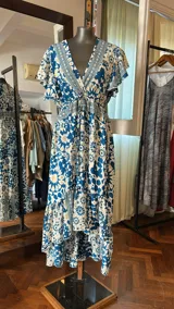 Vestido largo de seda con estampado floral en tonos azules y beige, escote en V, mangas cortas con volados y falda con volados escalonados.