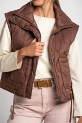 Chaleco marrón acolchado con cuello alto, cierre frontal con broches a presión y dos bolsillos delanteros con cordón ajustable.