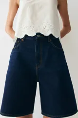 Bermuda de denim azul oscuro, de tiro alto y corte recto, con cinco bolsillos, cierre frontal con botón y trabillas para cinturón.