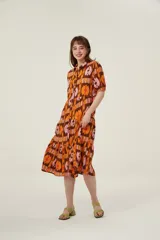 Vestido midi con estampado abstracto en tonos marrón, naranja y rosa. Tiene cuello camisero, mangas cortas abullonadas y falda escalonada con volantes.