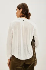 Camisa blanca de manga larga con cuello mao y escote en V. Presenta bordados florales en blanco y dorado en el frente.