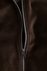 Campera corta de velour marrón oscuro, con cuello elevado, cierre frontal y bolsillos insertados al bies. Presenta elástico fruncido en puños y bajo.