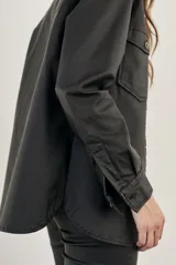 Sobrecamisa negra de textura simil cuero, con cuello camisero, cierre frontal con botones, mangas largas con puños abotonados, dos bolsillos con solapa en el pecho y corte recto.
