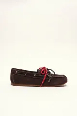 Mocasín tipo boat shoe color marrón oscuro, confeccionado en cuero, con cordones decorativos en rojo y blanco, y ojales dorados.