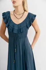 Vestido largo negro sin mangas, con escote redondo, espalda baja y volados en el escote. Ajuste en la cintura con cordón y terminaciones metálicas.