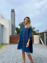 Camisola tipo poncho en jean azul oscuro con cuello camisero, cierre frontal con botones, mangas cortas amplias con volados y ruedo con flecos.