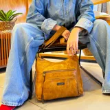 Bandolera negra de cuero sintético con dos bolsillos frontales con cierre, apertura superior con cierre, bolsillos internos con cierre y abiertos, bolsillo trasero con cierre y correa larga regulable a tono.