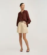 Short de mujer color beige claro, de cintura alta y corte holgado, con pliegues frontales y cierre tradicional. Incluye un cinturón fino de material sintético marrón.