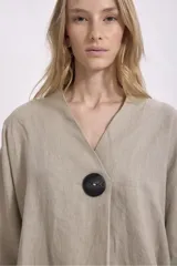 Blusa color crema de lino, de corte holgado, con cuello en V, mangas anchas y un botón grande negro.
