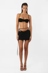 Minifalda negra de microfibra con tiro bajo, corte ajustado y frunces en el delantero. Incluye panty de microtul unida a la falda mediante tiras y argolla.