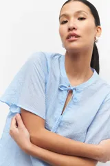 Blusa celeste a rayas verticales con cuello mao, mangas cortas y lazo en el frente.