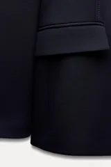 Blazer negra entallada con cuello solapa, manga larga con hombreras, bolsillos delanteros con solapa y cierre frontal con botones dorados.