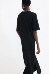 Vestido largo negro de punto suave, corte recto, cuello redondo, mangas cortas y tajo lateral pronunciado.