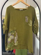 Blusa de lino color verde oliva, con mangas cortas enrollables y detalle de parche estampado floral en el frente y en el bolsillo.