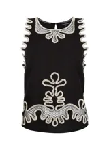 Blusa negra sin mangas con cuello redondo y detalles bordados en contraste color crudo en cuello, sisas y bajo. Presenta apliques ornamentales en el centro de la parte delantera y trasera, detalles calados con transparencias y abertura en forma de lágrima en la espalda con cierre de un botón.