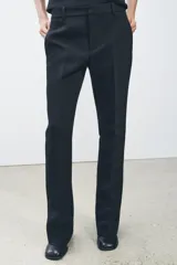 Pantalón negro de tiro medio con cintura con trabillas y corte flare. Cierre frontal con cremallera, botón y gancho metálico.