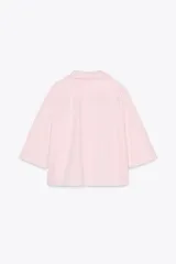 Camisa corta color rosa claro, confeccionada en algodón. Tiene cuello solapa de muescas, manga corta, bolsillo de plastrón en el pecho, bajo recto y cierre frontal con botones.