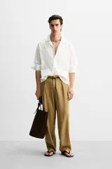 Camisa blanca de corte relaxed fit confeccionada en tejido de algodón y lino. Tiene cuello bowling, manga larga con puños abotonados, jaretas en el delantero, bolsillos de parche en pecho y cadera, bajo con aberturas laterales y cierre frontal con botones.