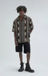 Camisa de manga corta tejida en punto abierto (símil crochet), con calce oversize. Presenta un patrón geométrico en tonos negro, marrón y blanco.