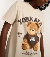 Remera color crema de algodón con cuello redondo y mangas cortas. Presenta un estampado de un oso de peluche con una sudadera que dice "New York" y la inscripción "York Bears".