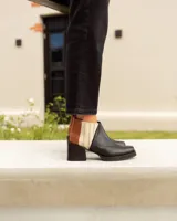 Botines Chelsea de cuero, color negro, con detalles en cuero marrón texturizado (tipo cocodrilo) y paneles laterales en color beige claro. Tienen un taco ancho y cuadrado, y cierre de cremallera lateral en color beige.