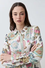 Camisa de manga larga con estampado de arabescos en tonos rosa, celeste, marrón y verde agua sobre fondo blanco. Tiene cuello clásico y cierre con botones.