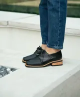 Zapato acordonado de cuero vacuno color marrón oscuro, con suela de goma, horma cuadrada y tacón bajo.