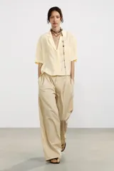 Camisa color amarillo pálido de tejido fluido, con cuello solapa, escote pico, manga corta, bolsillo de parche en el pecho y cierre frontal con botones.