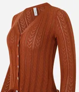 Cárdigan de punto color marrón óxido con diseño calado, cuello en V, cierre frontal con botones blancos, mangas largas con volados en los puños y volados en el ruedo.