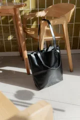 Bolso tote negro de cuero con doble asa de hombro. Interior sin forro con bolsillo para celular y cierre con broche central.