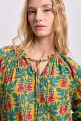 Blusa de manga larga con estampado floral en tonos mostaza, verde y rosa. Tiene cuello redondo con lazo ajustable.