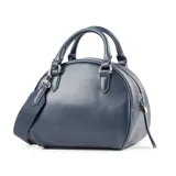 Cartera tipo baúl color azul, con diseño tejido en símil cuero. Tiene doble asa corta, correa larga regulable y herrajes plateados. El acceso es con cierre y cuenta con un bolsillo interno con cierre y dos abiertos.