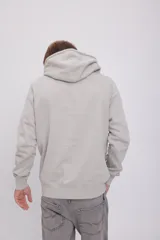 Hoodie tipo canguro color gris mineral, de manga larga con capucha y fit regular. Cuenta con un bolsillo y estampado de goma con tacto suave. Tejido Loop Back.