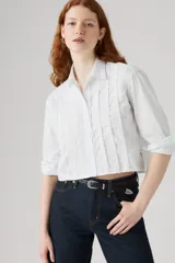 Camisa cropped blanca de manga larga con detalles de volados y pliegues verticales en el frente.