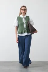 Chaleco tejido de punto color beige con trama texturada y diseño liviano. Presenta cuello a la base, silueta recta y cierre frontal mediante tres lazos delicados.