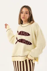 Sweater color manteca de tejido de punto con cuello redondo y ribete marrón. Presenta dos peces marrones tejidos en el frente con detalles bordados a mano.