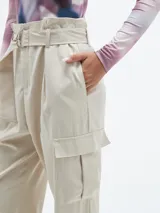 Pantalón color beige claro, de corte holgado, con bolsillos laterales y cinturón con hebilla metálica.