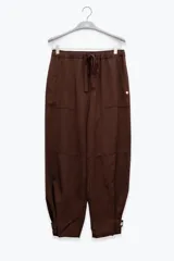Pantalón marrón de lino y tencel, corte holgado, con cintura elástica ajustable con cordón, bolsillos laterales y detalle regulable con botón en los tobillos.
