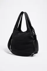 Bolso tipo shopper de nylon negro, con estructura blanda y acabado ligeramente arrugado. Cuenta con doble asa de mano y una correa ajustable y extraíble para llevar al hombro o cruzado. Presenta bolsillos exteriores con cierre de cremallera a cada lado y el logo metálico de Bimba y Lola en la parte inferior frontal.