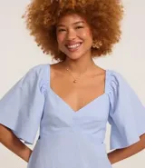 Vestido corto evasê de viscolino color crudo, con escote en V, mangas cortas amplias, recorte cut-out en los laterales de la cintura y volado en el ruedo.